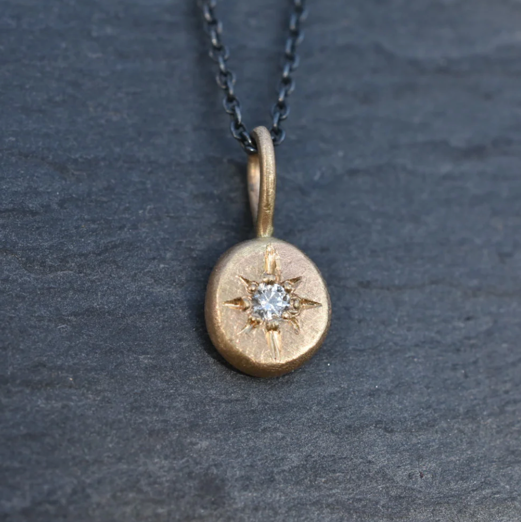 Gold pendant with a central diamond on a dark gray background