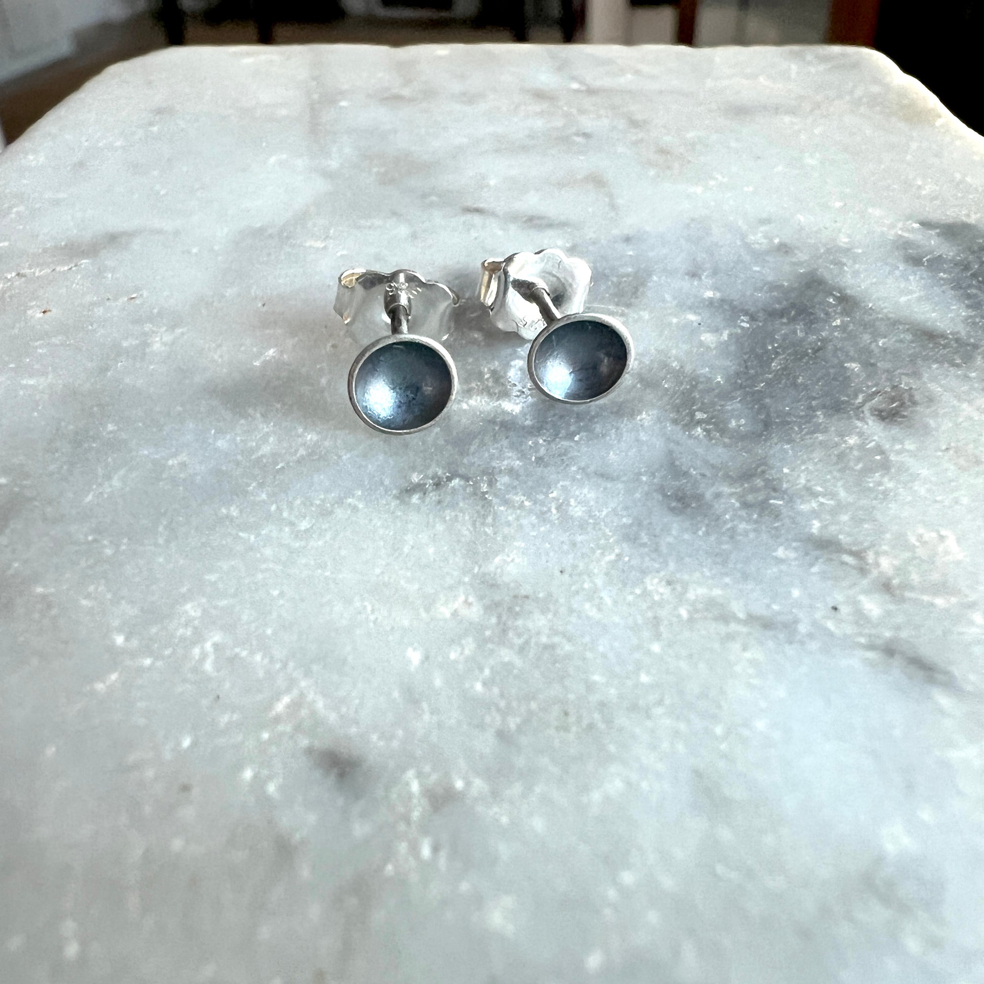 Pair of silver earrings with black centers on a marble surface
