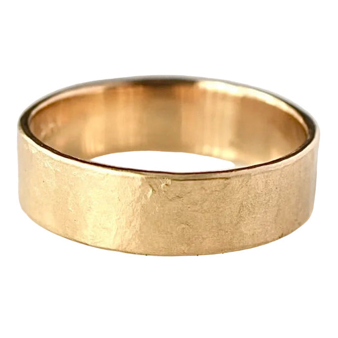 A hammered yellow gold band ring resting on a light gray marble surface.