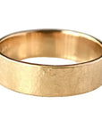 A hammered yellow gold band ring resting on a light gray marble surface.