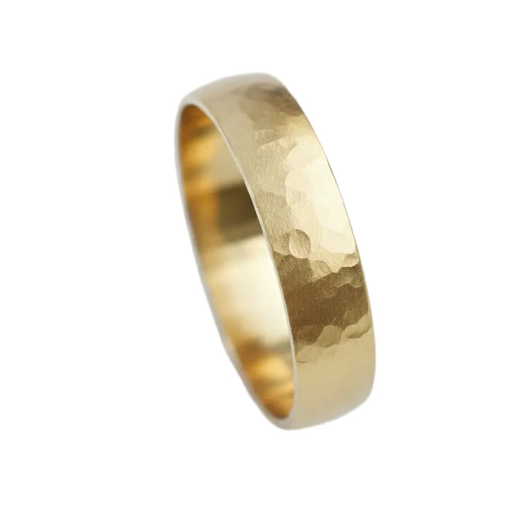 A hammered gold band ring photographed on a soft light blue background.