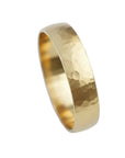 A hammered gold band ring photographed on a soft light blue background.